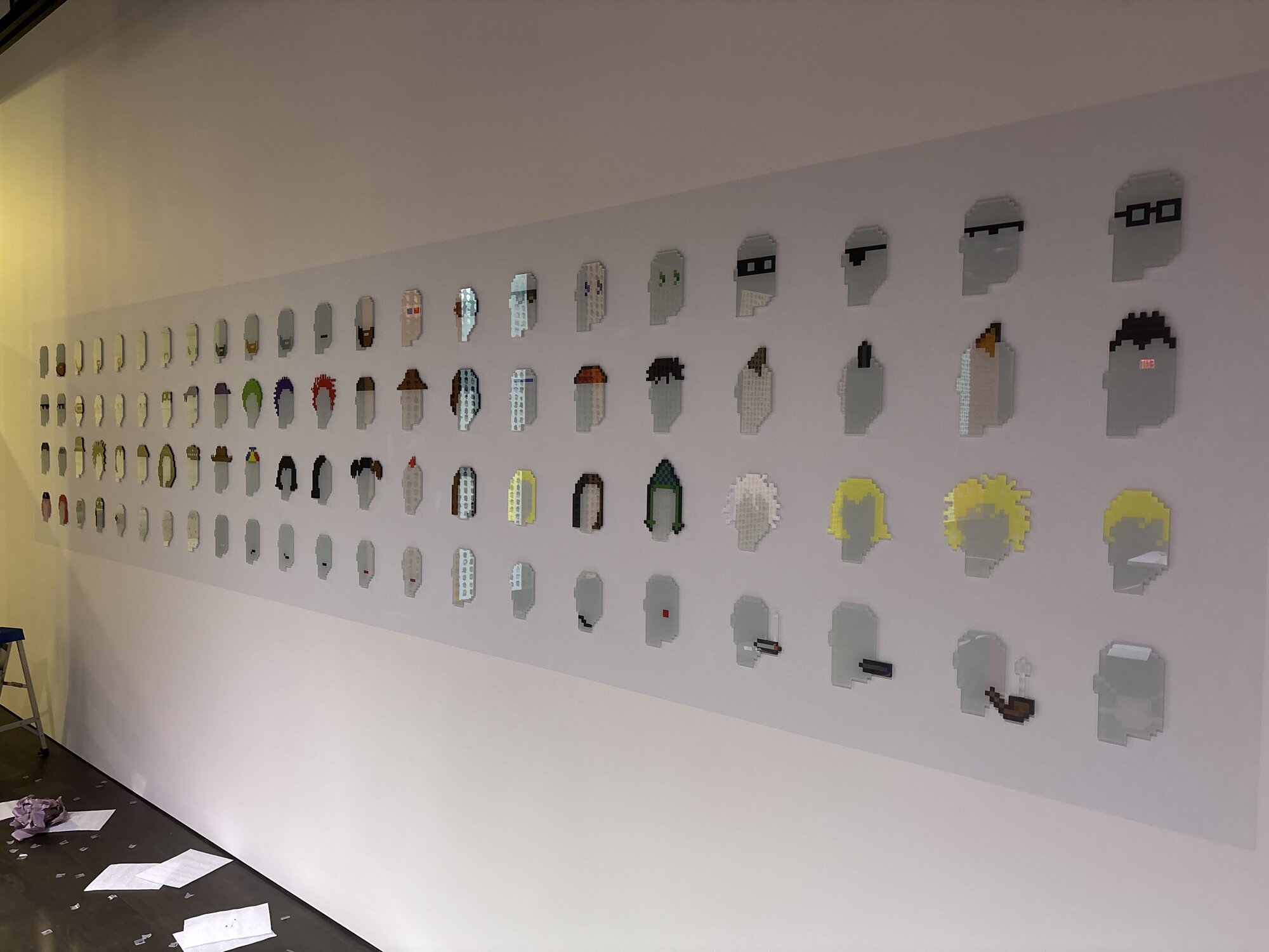 On-site installation — a long gallery wall of mounted pixel-art portrait panels, installed and aligned in rows